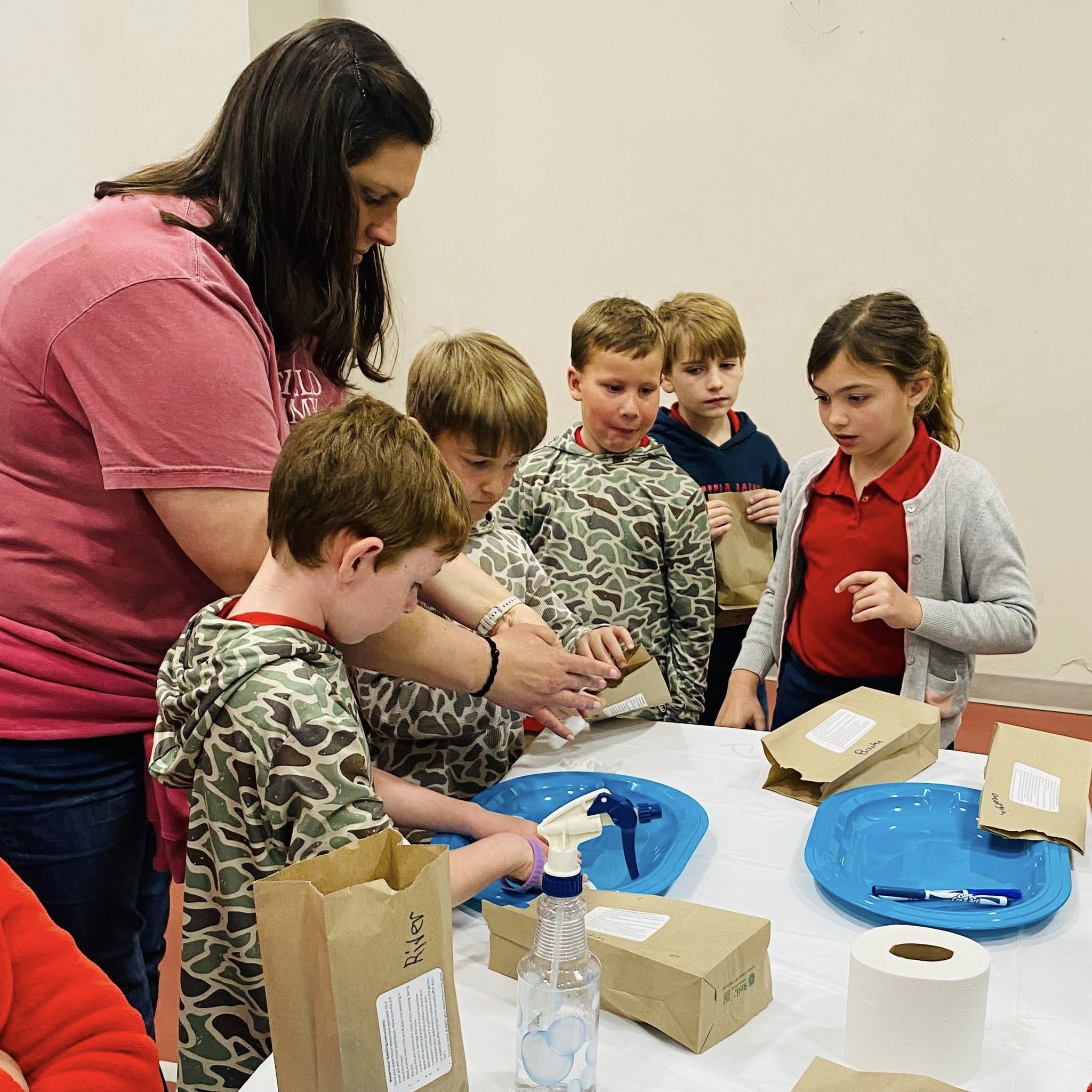 A woman helping kids put something in a small paper bag.
